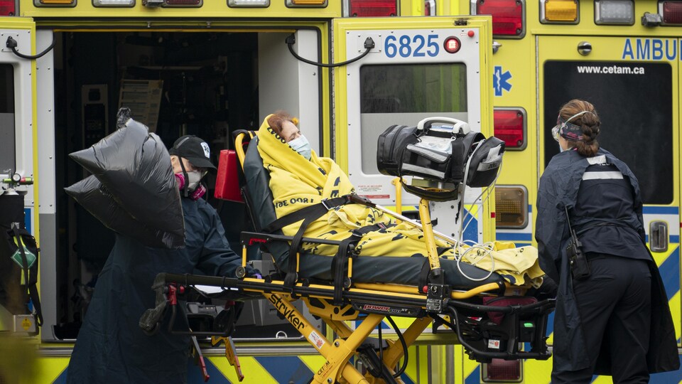 Deux ambulanciers s'occupent d'une personne allongée sur une civière.