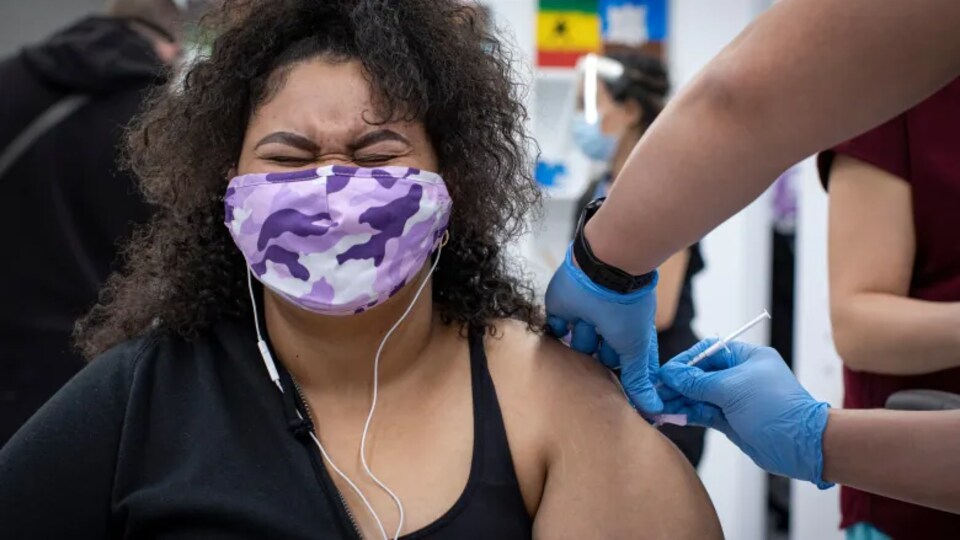 Une femme ferme les yeux très fort en se faisant vacciner.