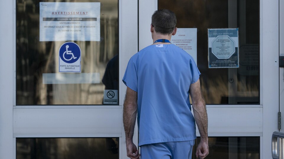 Un préposé, de dos, s'apprête à franchir les portes d'entrée d'un CHSLD.