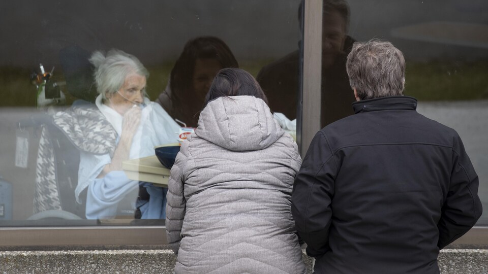Des visiteurs regardent une patiente par la fenêtre du CHSLD Éloria-Lepage, à Montréal.