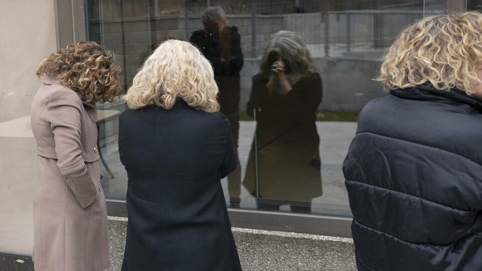 Trois femmes et un homme en pleurs se cachent le visage de leurs mains, peinés, devant la fenêtre d'un centre de soins de longue durée.
