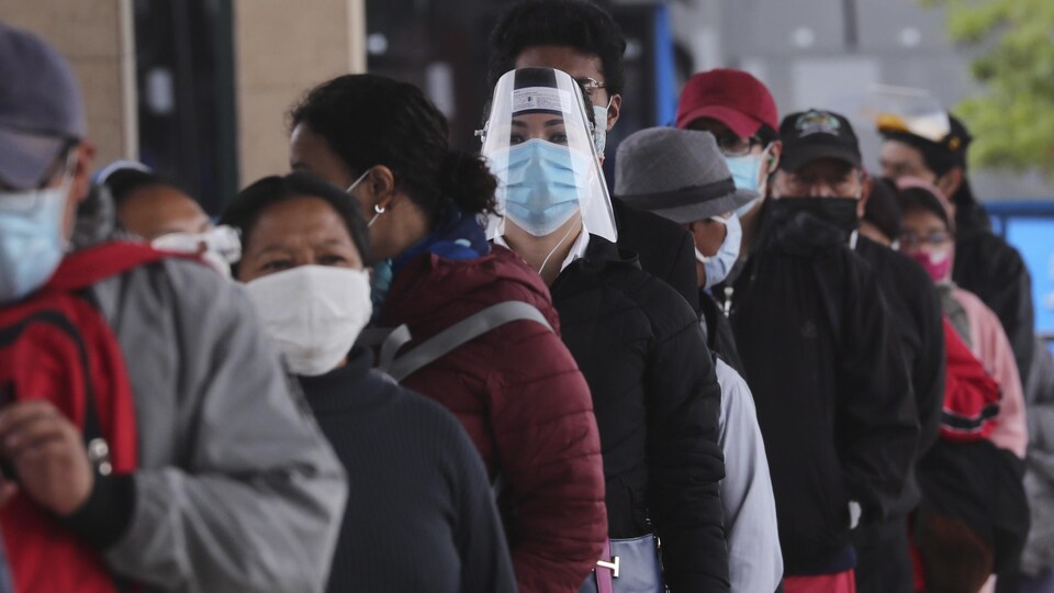 Des gens en file portent le masque de protection.