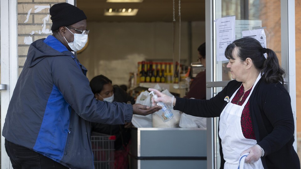 Une femme tend du gel désinfectant à un homme voulant entrer dans un magasin.