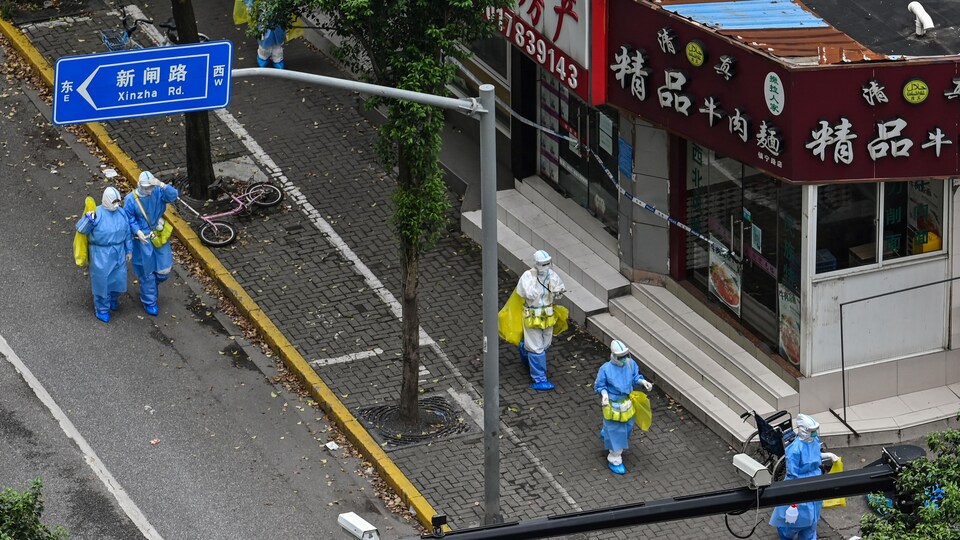 Des travailleurs de la santé vêtus de combinaison sanitaire marchent dans un quartier de Shanghai.