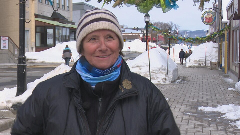 Claudine Roy debout dehors dans une rue commerciale en hiver.