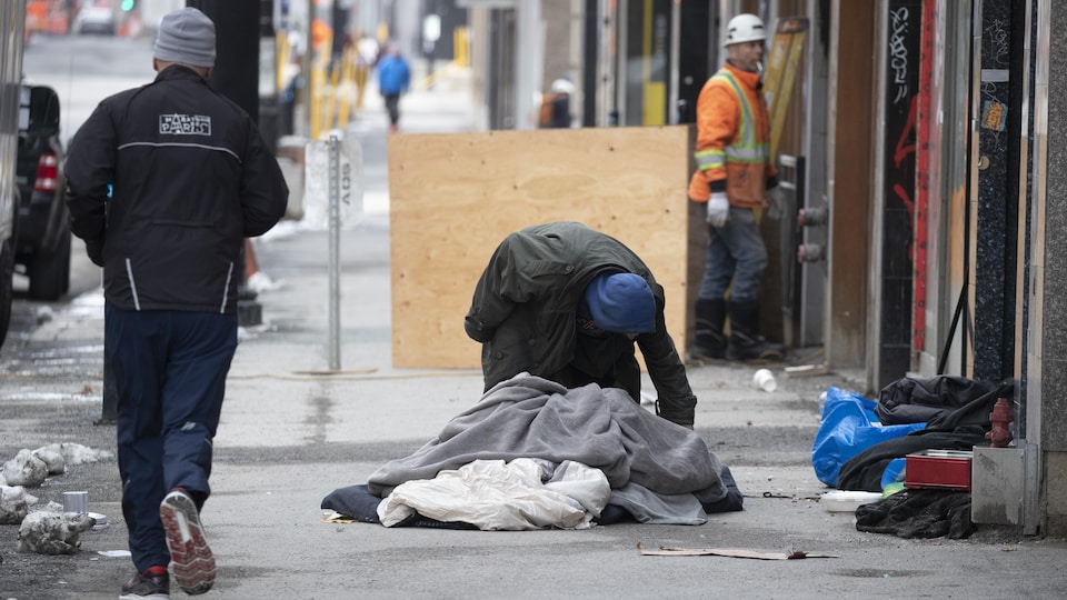 Un sans-abri ramasse ses affaires sur un trottoir de Montréal.