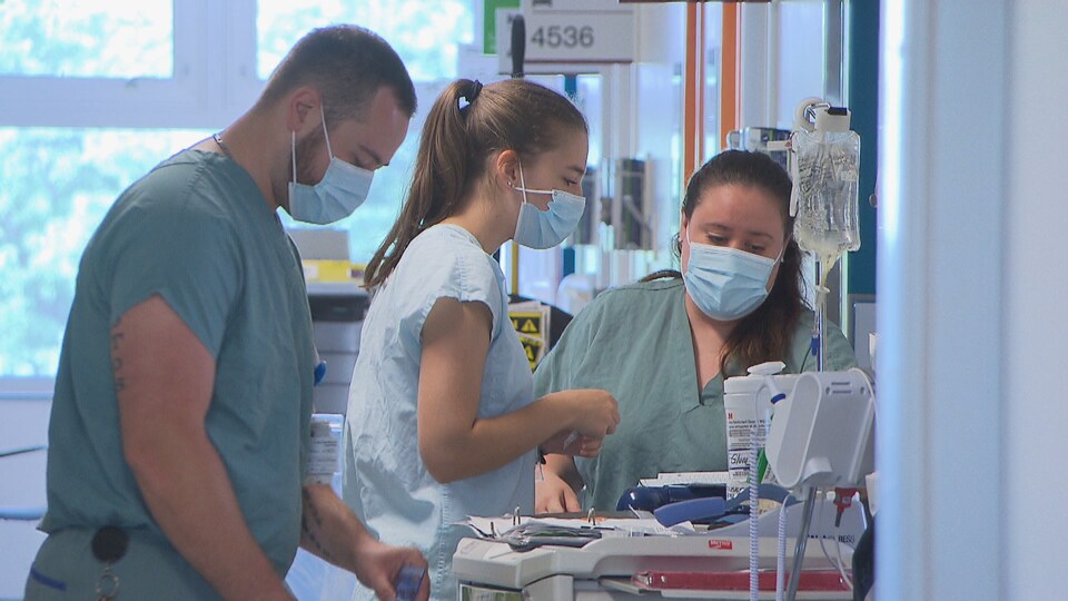 Trois infirmiers sont en train de se préparer à entrer dans une chambre d'un patient.Tous portent un masque.