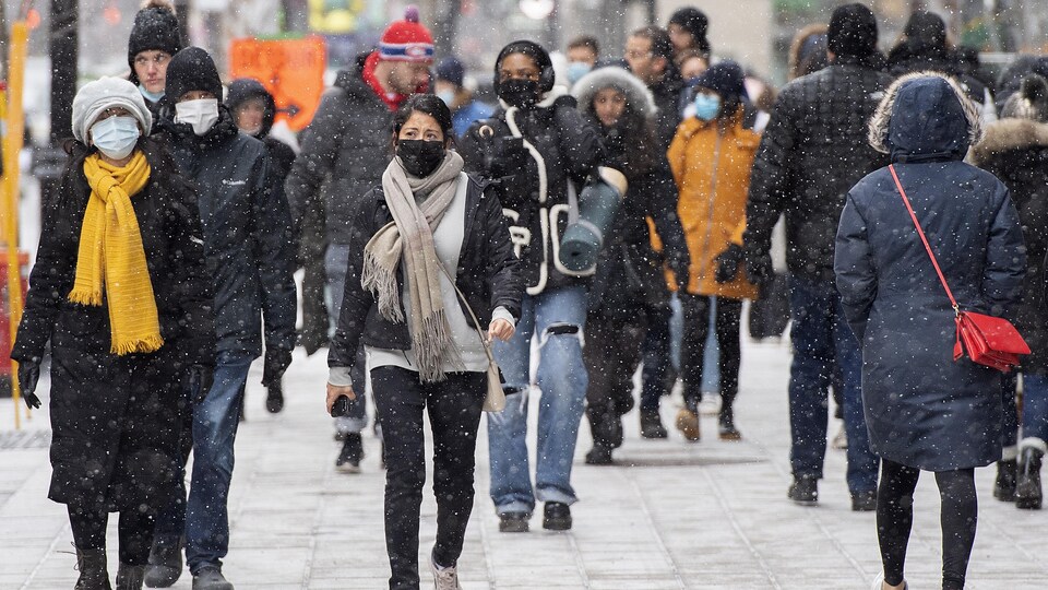 Des gens marchent sur un trottoir en ville. Plusieurs sont masqués.