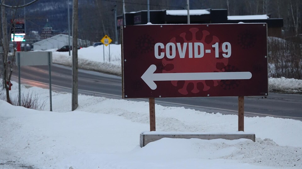 Une pancarte COVID-19 rouge avec de la neige et une route déserte en arrière-plan.