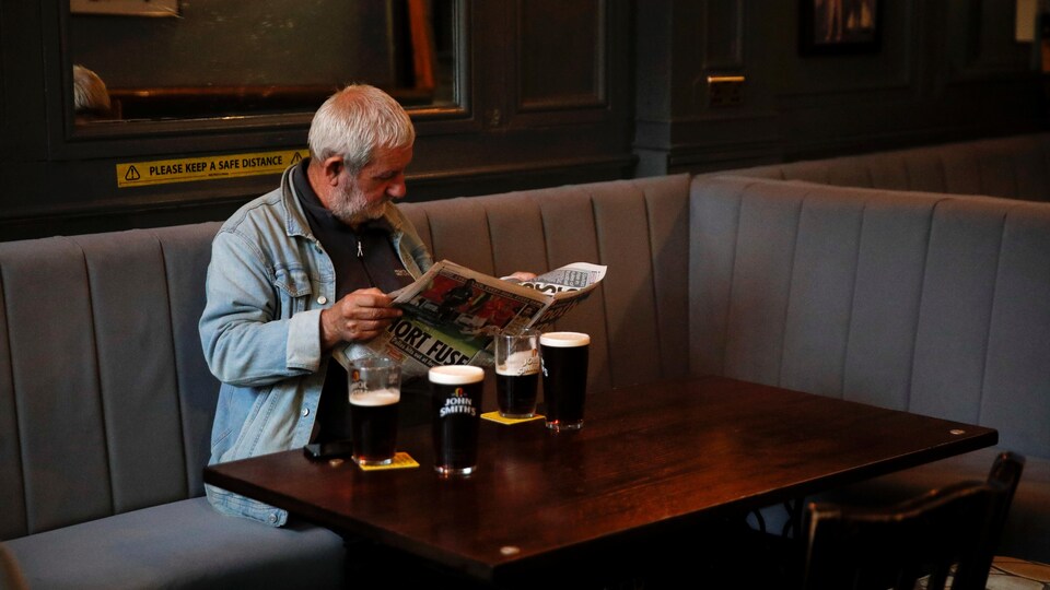 Un homme est assis et lit le journal devant quatre pintes de bière.
