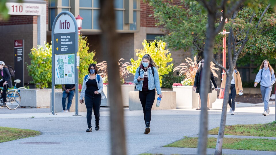 Les étudiants qui marchent sur le trottoir portent des masques.
