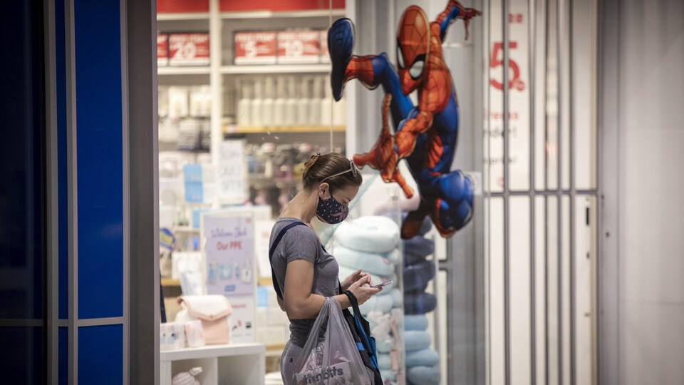 Une cliente qui porte un masque consulte son téléphone devant une décalque de Spiderman au Centre Eaton de Toronto.