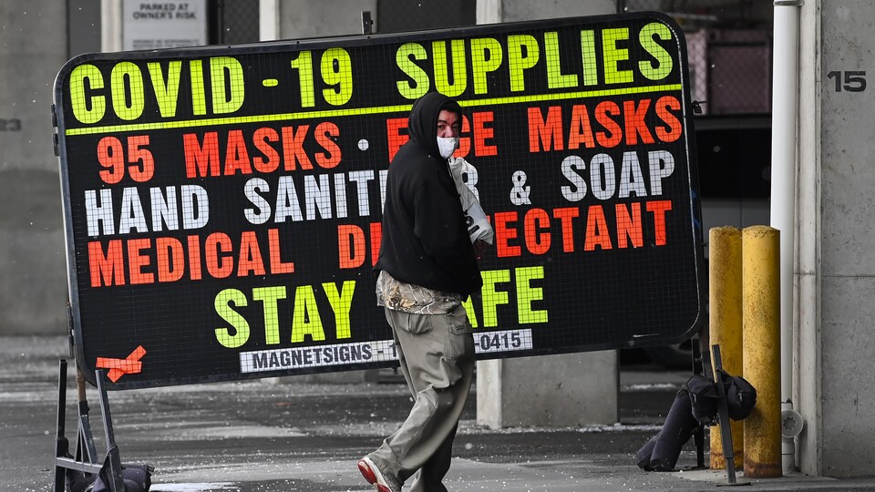 Un homme marche devant l'affiche d'un magasin qui vend des fournitures pour lutter contre la COVID-19.