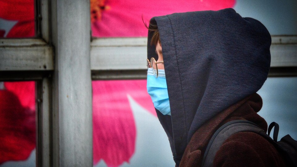 Un passant portant un masque, des lunettes, un chandail à capuchon et un sac-à-dos.