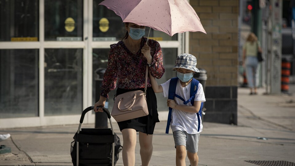 Une mère et son enfant portant un masque sur le trottoir.