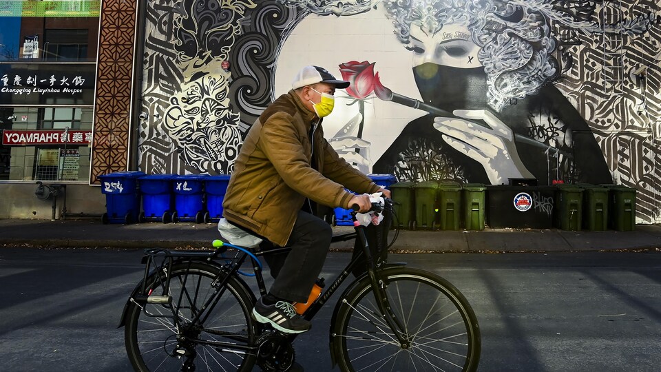 Un cycliste passe devant la murale d'une femme portant un masque qui peint une rose à Toronto.