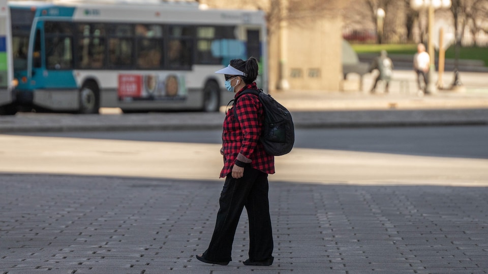 Une femme marche dans la rue avec un masque au visage.