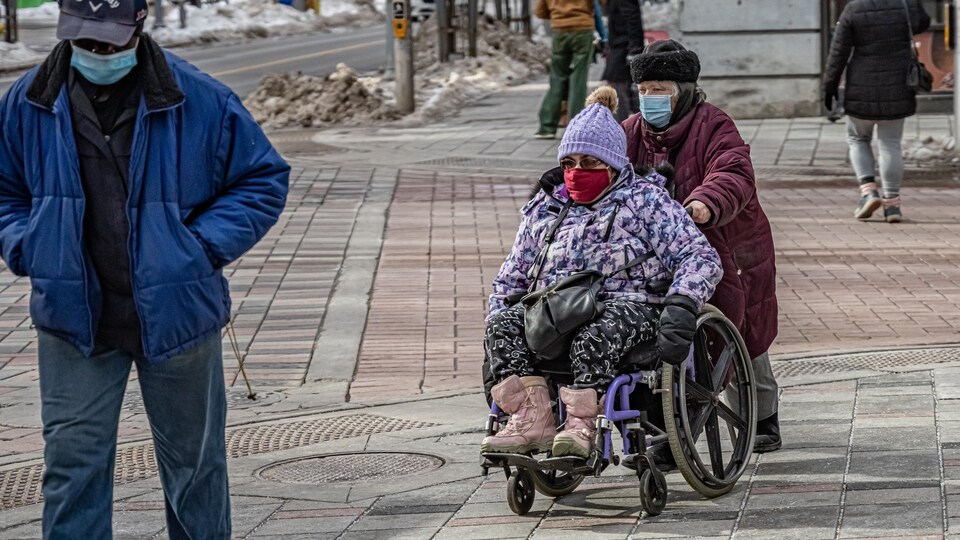 Un proche-aidant pousse une personne en fauteuil roulant dans la rue.
