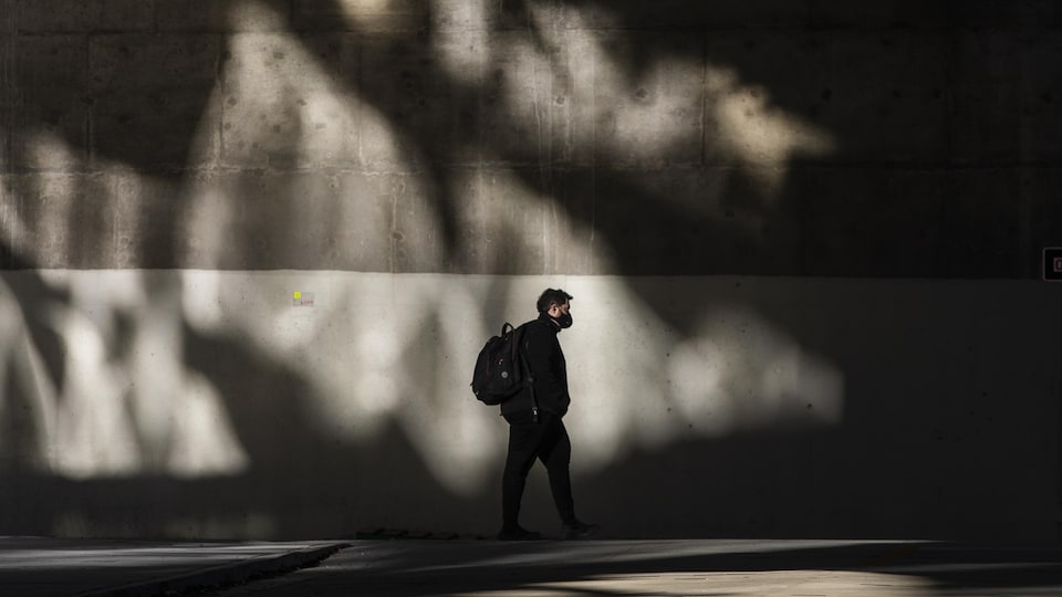Un homme porte un masque et marche le long d'un mur de béton à Vancouver.