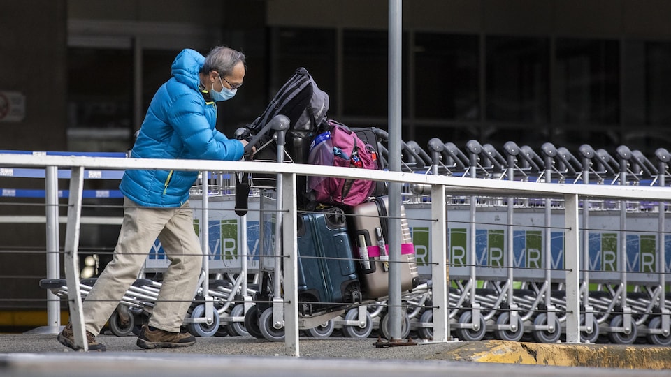 Un passager poussant un chariot à bagages à l'extérieur de l'aéroport.