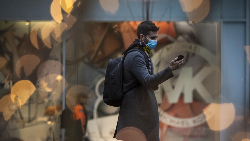 Un homme porte un masque et regarde son cellulaire dans une rue de Vancouver.
