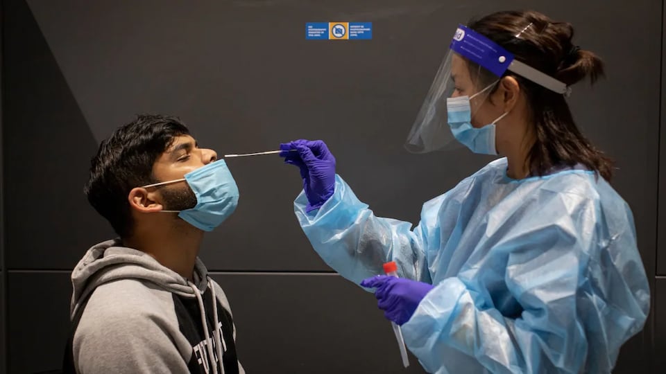Une personne se fait insérer un écouvillon dans le nez par une infirmière.