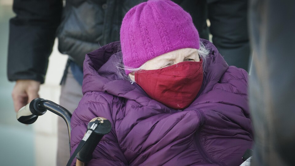 Une dame âgée porte bonnet, couvre-visage et manteau d'hiver.