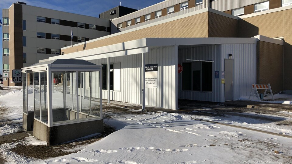 Un petit bâtiment couvert adjacent à un hôpital où peut pénétrer une voiture.
