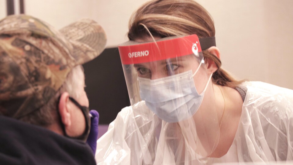Une femme qui porte de l'équipement de protection individuel prélève un échantillon pour un test de dépistage.