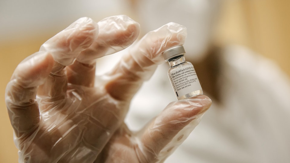 Un employé qui porte des gants en latex tient une dose du vaccin de Pfizer dans ses mains.