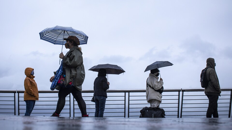 Des gens font la file sous la pluie.