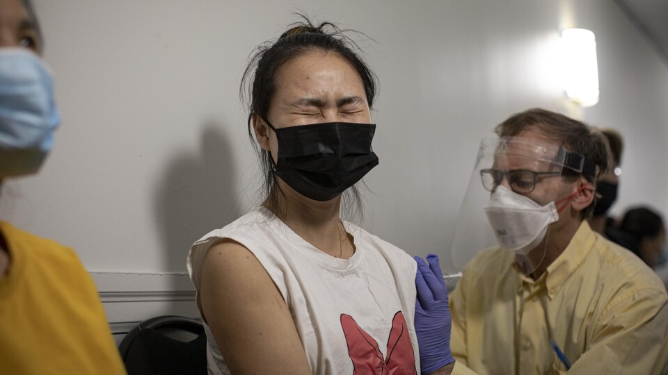 Une jeune femme au visage crispé reçoit un vaccin.