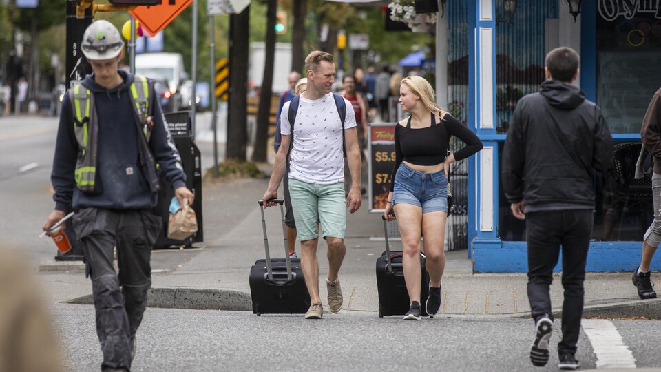 Deux personnes traversent une rue du centre-ville de Vancouver en portant une valise.