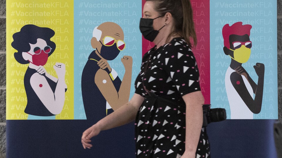 Une personne marche devant une murale de personnages masquées.