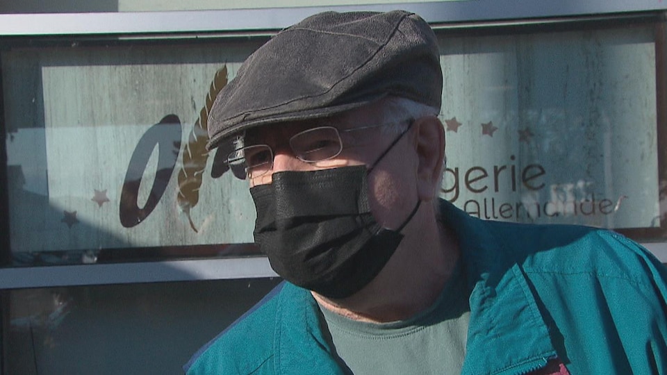 Un homme d'âge mûr portant des lunettes et coiffé d'une casquette, à l'extérieur d'un bâtiment.