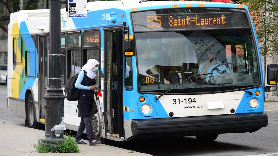 Une femme portant un masque s'apprête à monter dans un autobus.