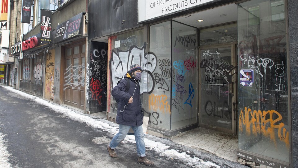 Un homme marche devant des commerces vandalisés et abandonnés.