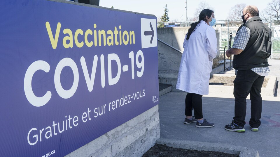 Une femme et un homme discutent devant l'entrée d'une clinique de vaccination.