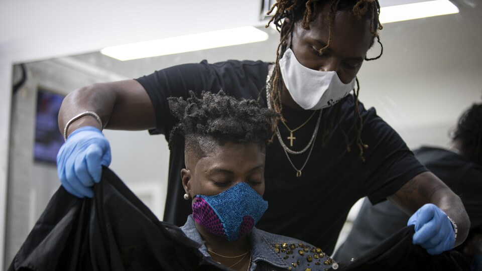 Un coiffeur qui porte un masque couvre une femme avant de lui couper les cheveux.