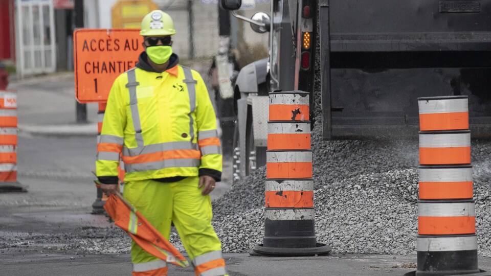 Un homme habillé tout en jaune et portant un masque se tient près d'un camion qui déverse du gravier.