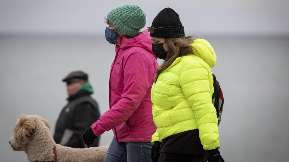 Deux femmes portant un masque promènent un chien.