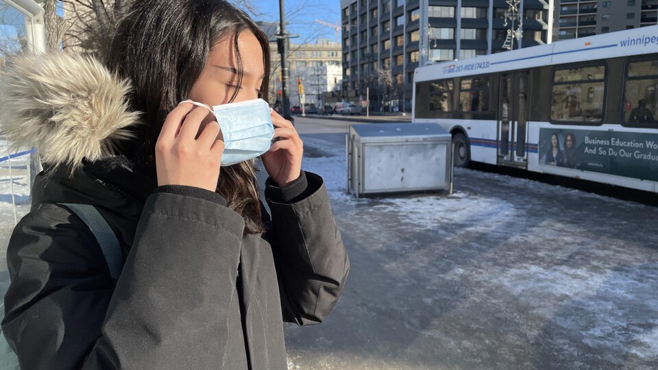Une femme enfile son masque contre la transmission de la COVID-19 le 13 décembre à Winnipeg.