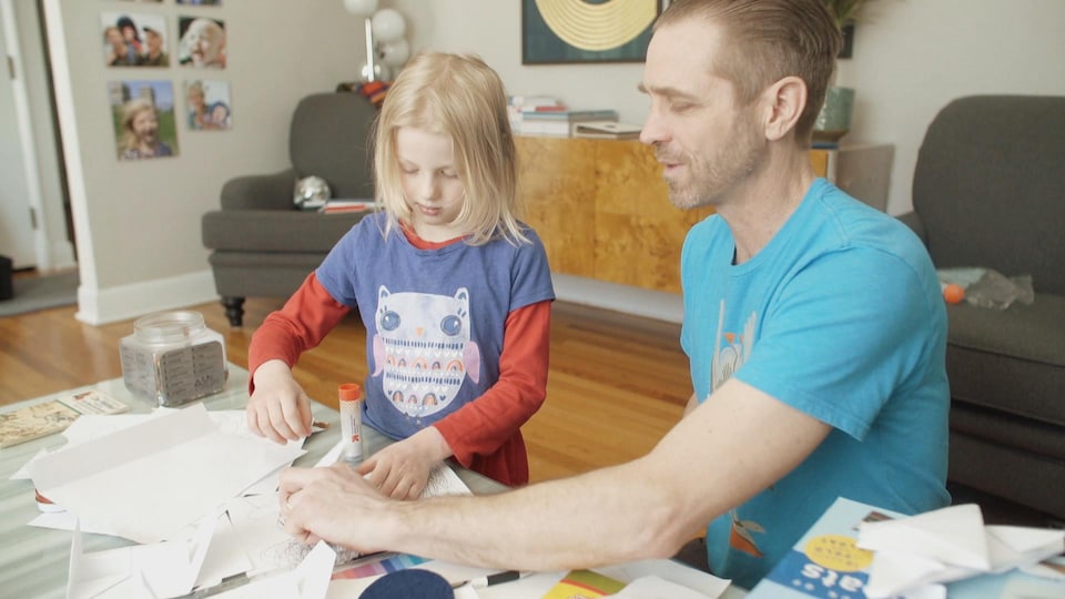 Un père et sa fille assis à la table du salon faisant l'école à la maison.