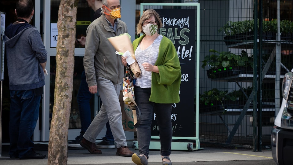Une femme et un homme portant un masque sortent d'un magasin Whole Foods.