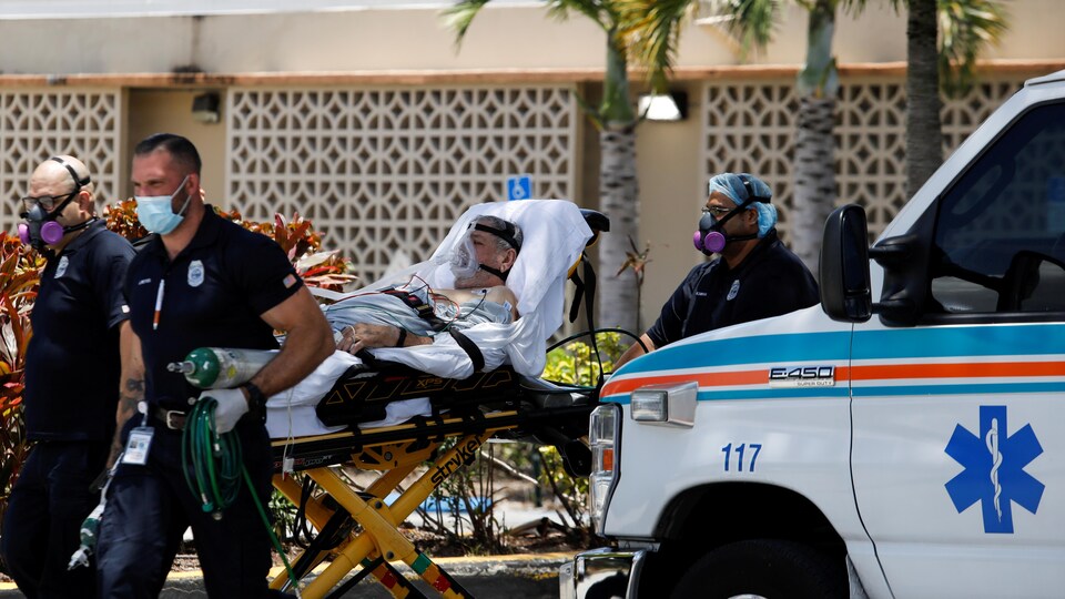 Trois ambulanciers poussent une civière sur laquelle un homme est couché. 