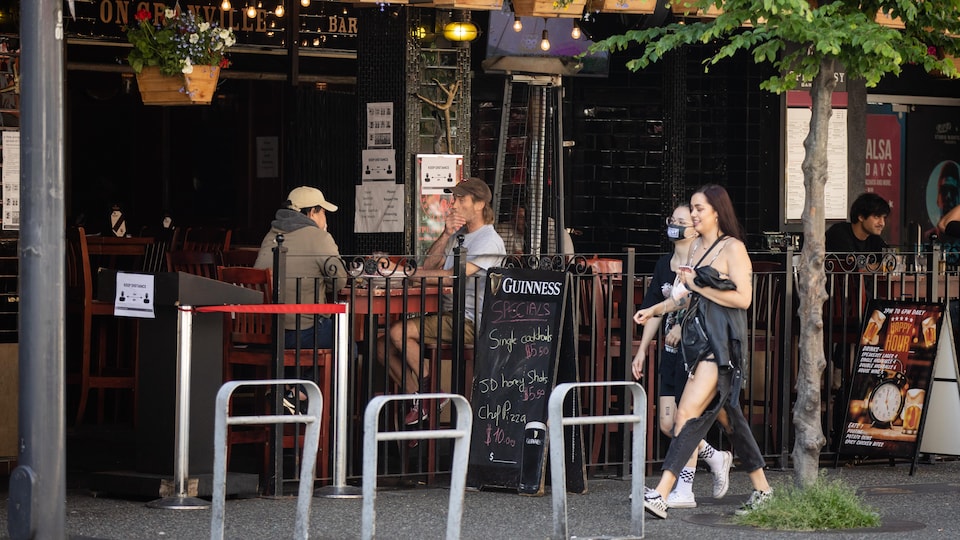 Des gens marchent sur un trottoir devant une terrasse de restaurant.