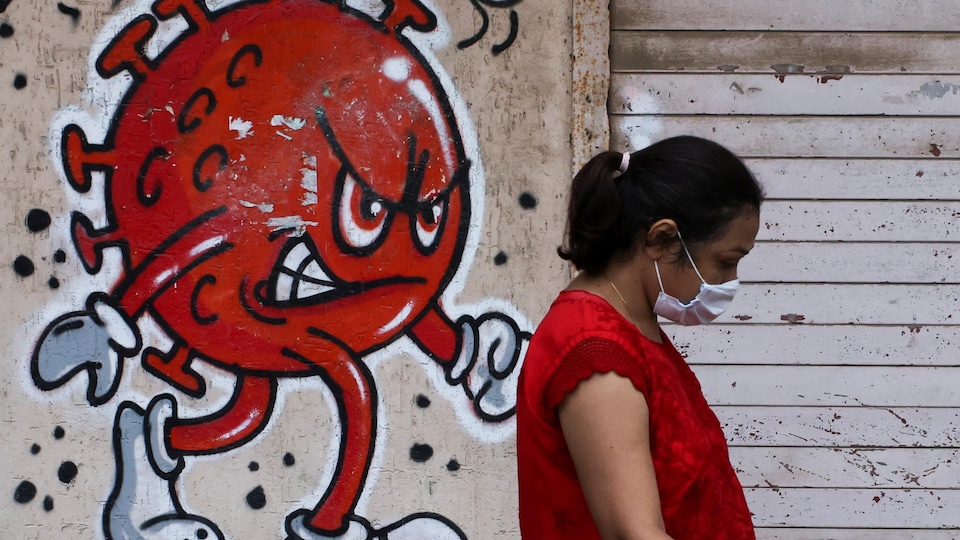 Une femme portant un masque marche devant un graffiti d'un virus menaçant.