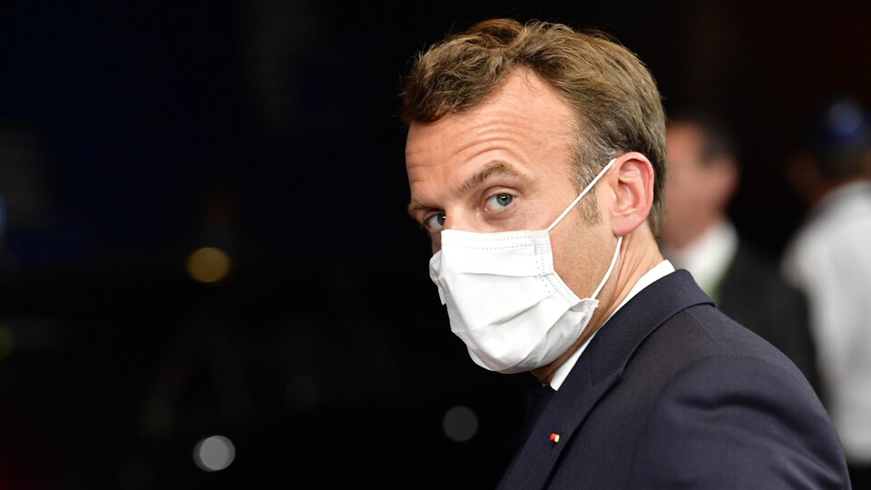 Masqué, le président français fixe l'appareil du photographe.