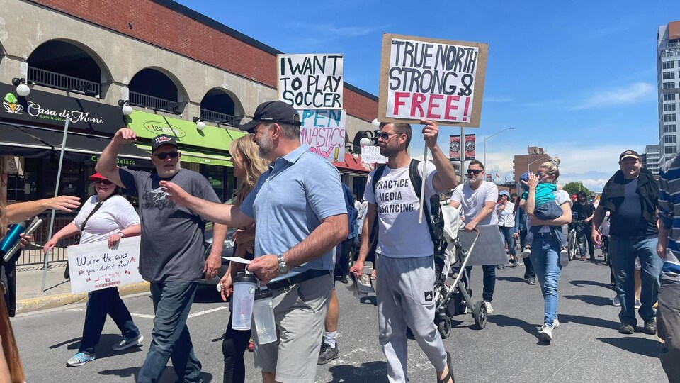 Des personnes marchent dans le marché By, sans masque et munis d'affiches.