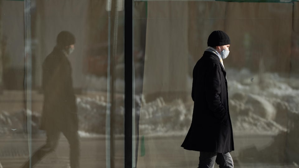 Un homme portant un masque marche sur un trottoir enneigé. 